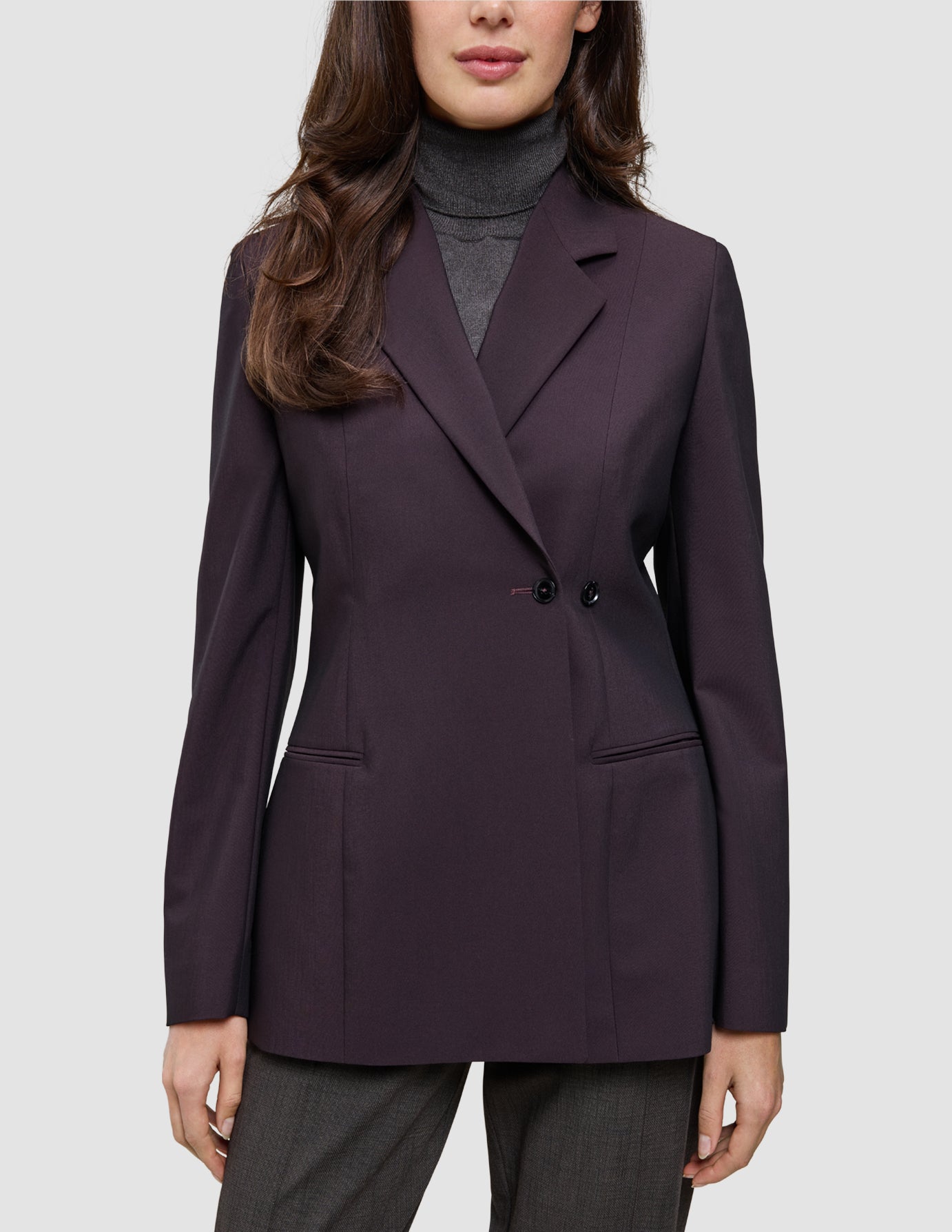 Eine Frau trägt einen dunkelvioletten Women’s Avira Blazer Burgundy Berry im klassischen skandinavischen Zweireiher-Design über einem grauen Rollkragenpullover.